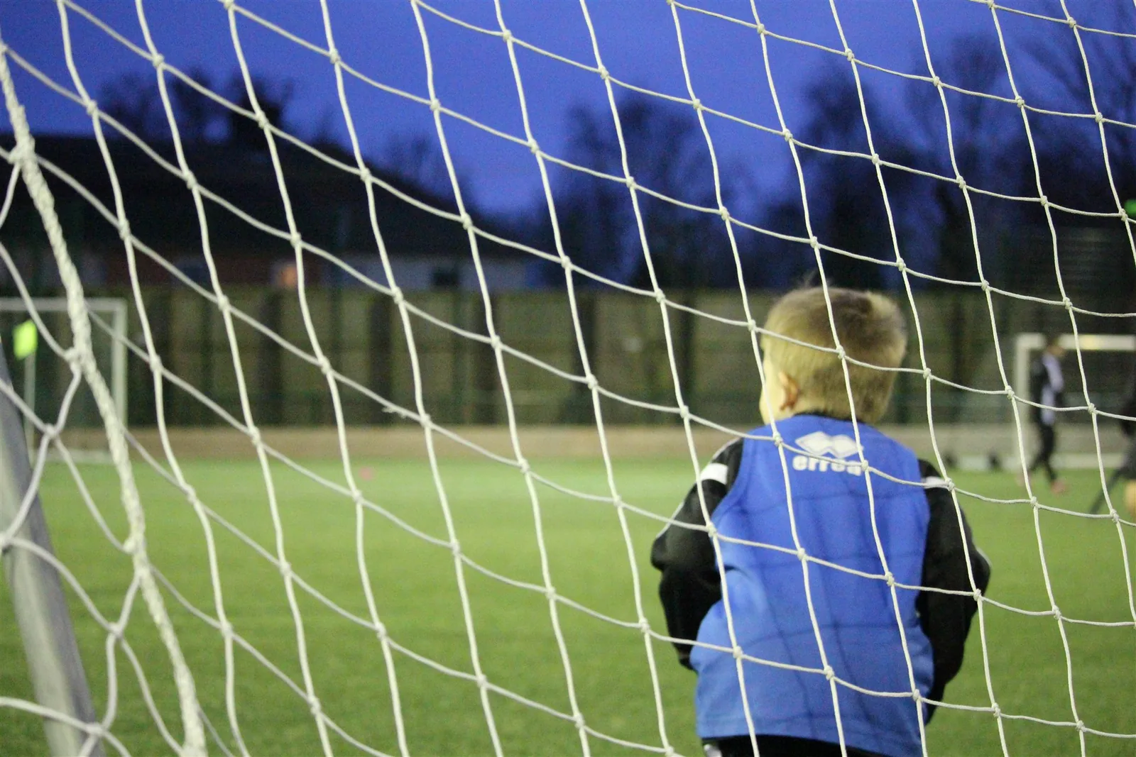 A young goalkeeper watching the game through the goal net