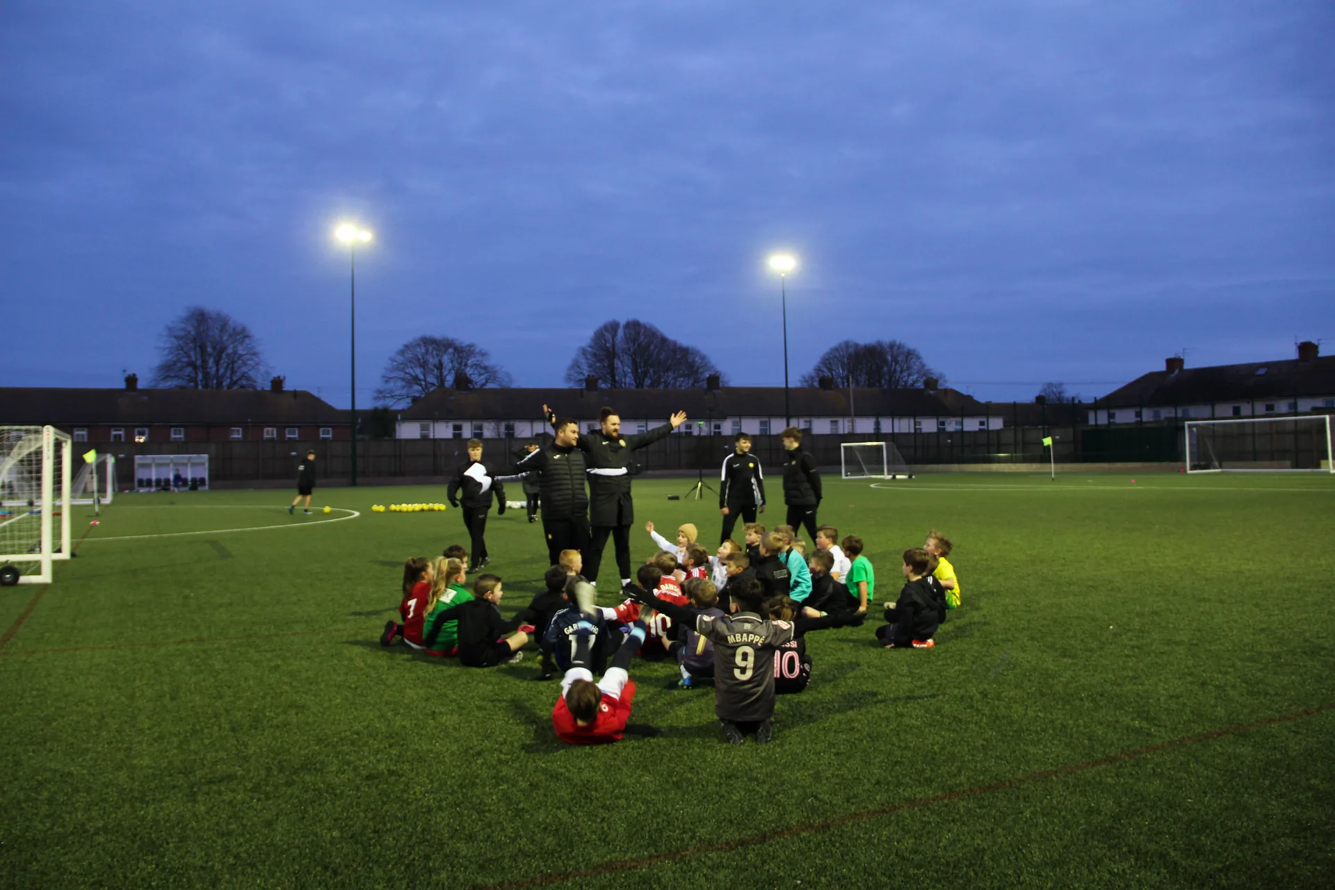 Coastal Ballers coaches speaking with young players during an evening football session at The Green